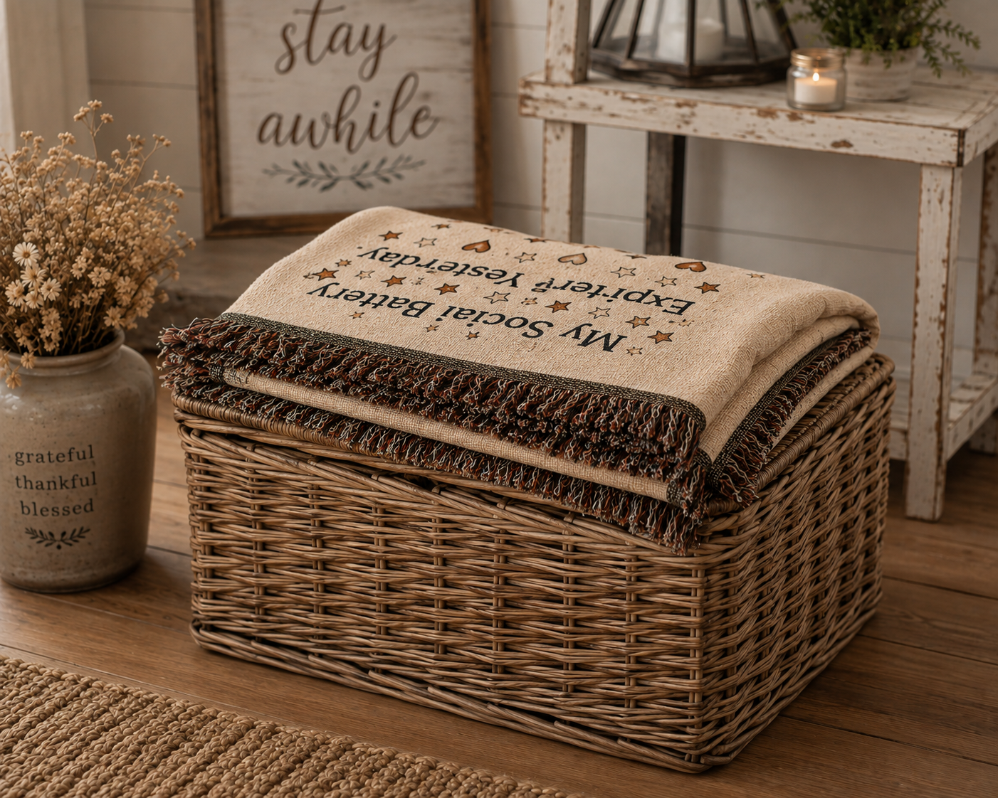 A woven wicker storage basket with a folded cream throw blanket featuring embroidered text and star motifs, styled in a rustic room setting.