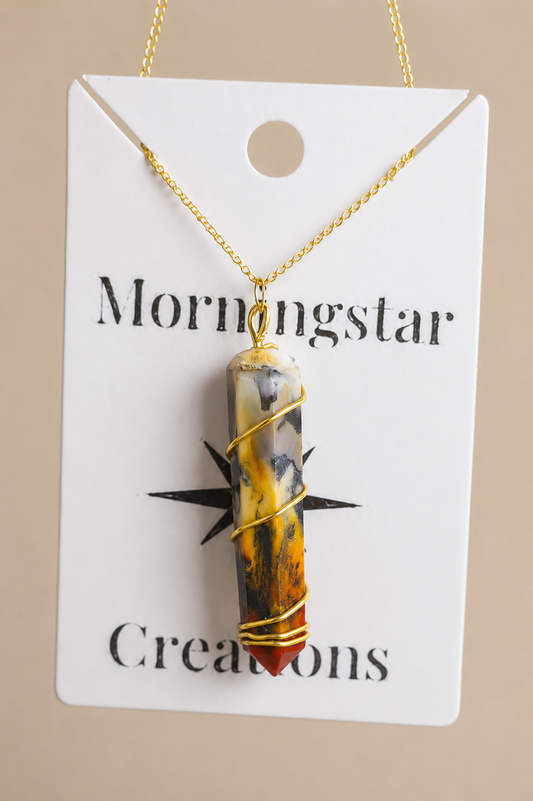A gold chain necklace with a marbled amber, yellow, and gray stone pendant wrapped in gold wire, displayed on a white card labeled 'Mornigstar Creations' against a beige background.