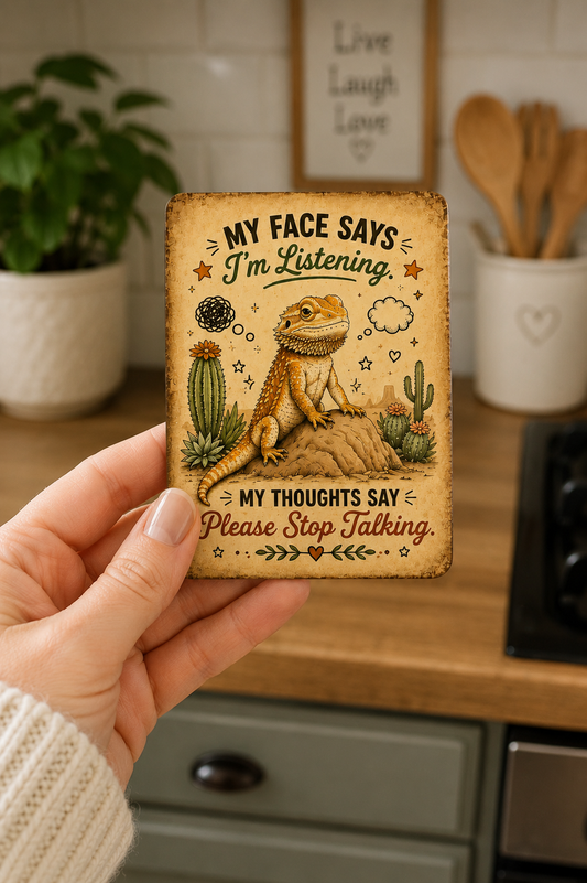 Person holding a decorative magnet with a bearded dragon illustration and humorous text in a kitchen setting.