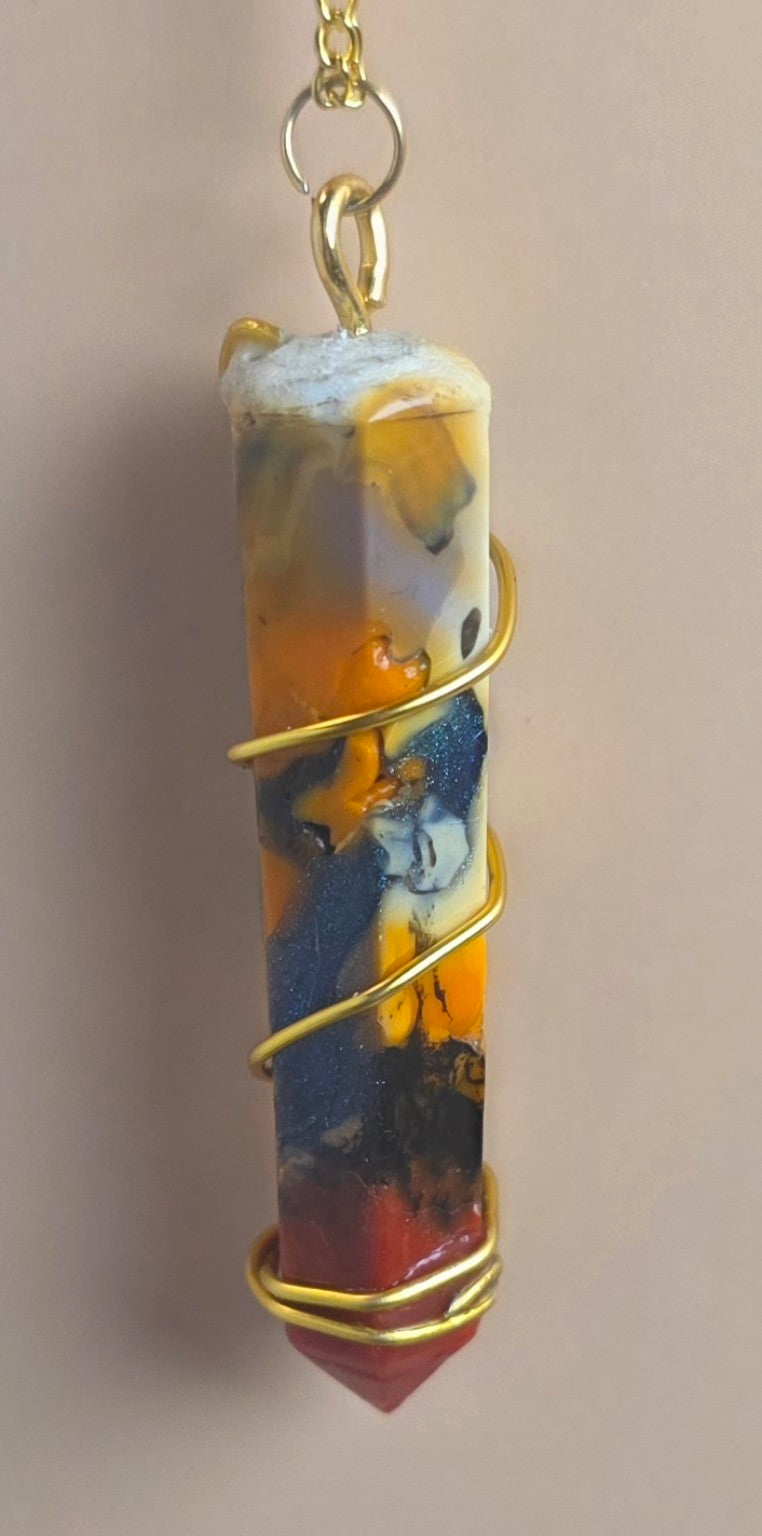 A cylindrical resin crystal pendant with a gold wire wrap and a gold chain, featuring an abstract marbled pattern of orange, yellow, blue, black, and red, set against a plain beige background.