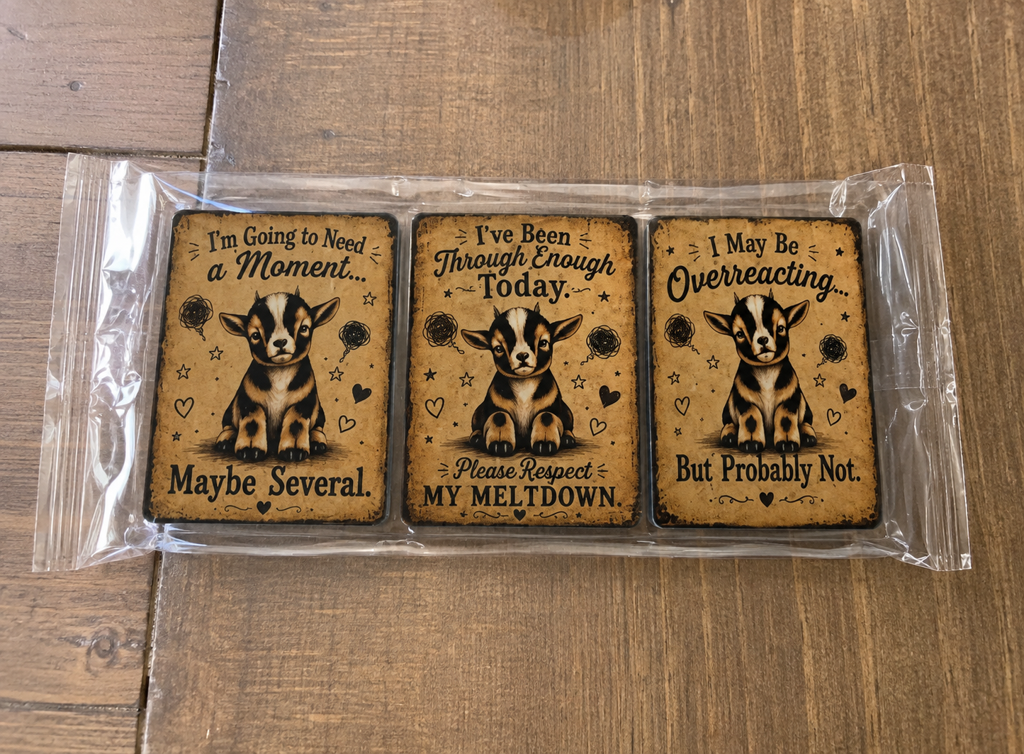Three rectangular goat with humorous dog-themed quotes and illustrations of small dogs, sealed in a clear plastic bag and placed on a wooden surface.