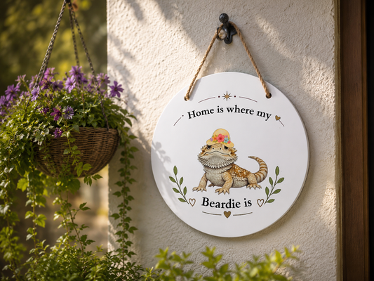 Decorative sign with a bearded dragon illustration and text 'Home is where my Beardie is' hanging on a wall with plants.