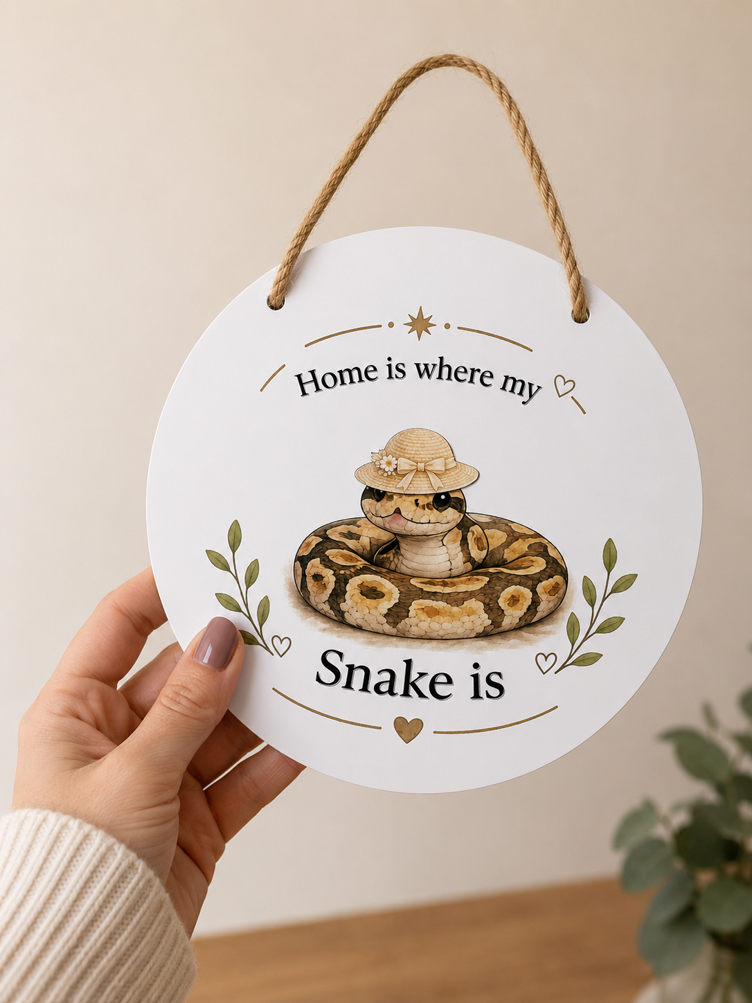 Round white sign with a snake illustration and text held by a hand against a beige background