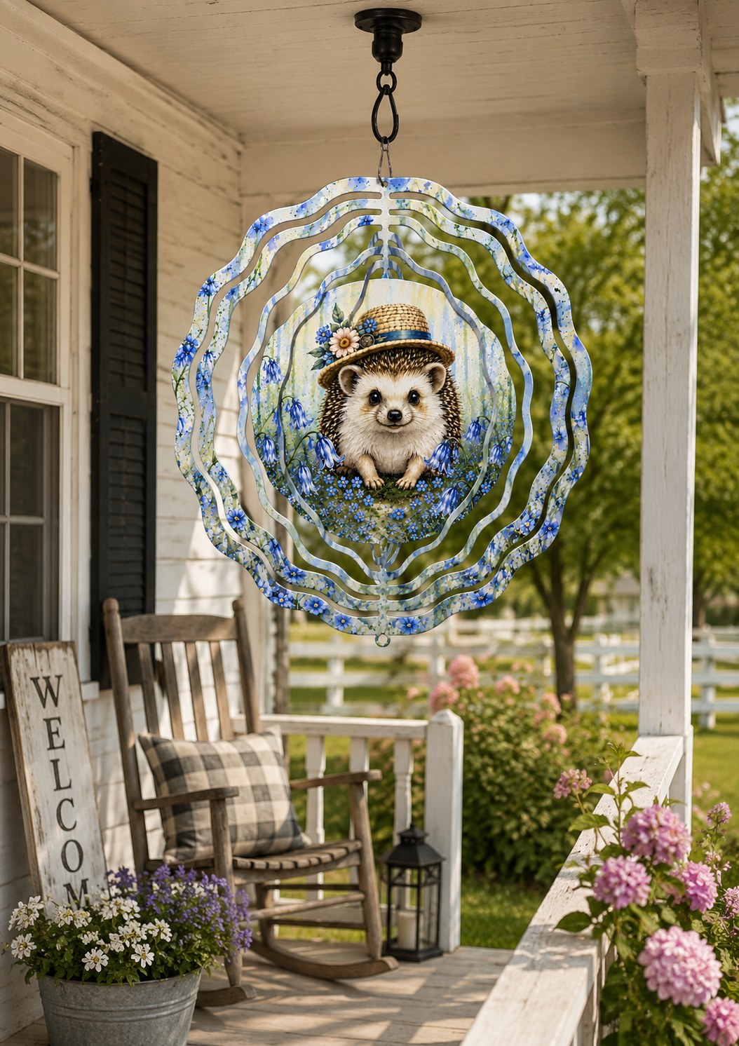 A decorative hanging metal wind spinner with a hedgehog illustration, displayed on a rustic white wooden porch with a rocking chair, flowers, and greenery in the background.