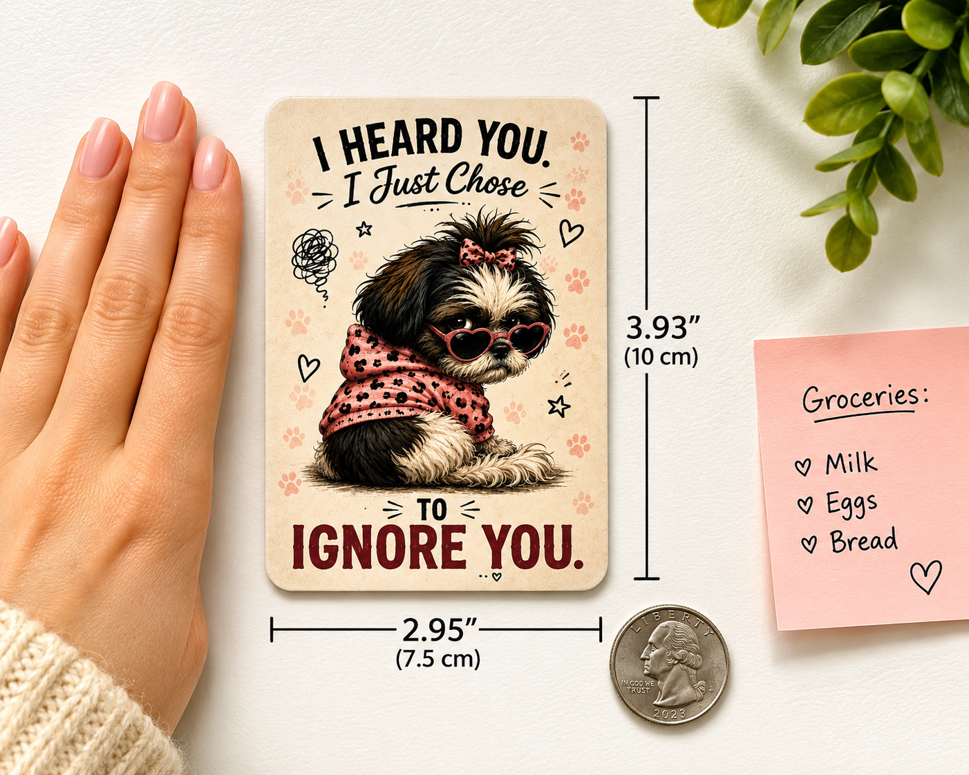 Card with a dog illustration and text, held by a hand next to a coin for scale, on a light surface with a plant.