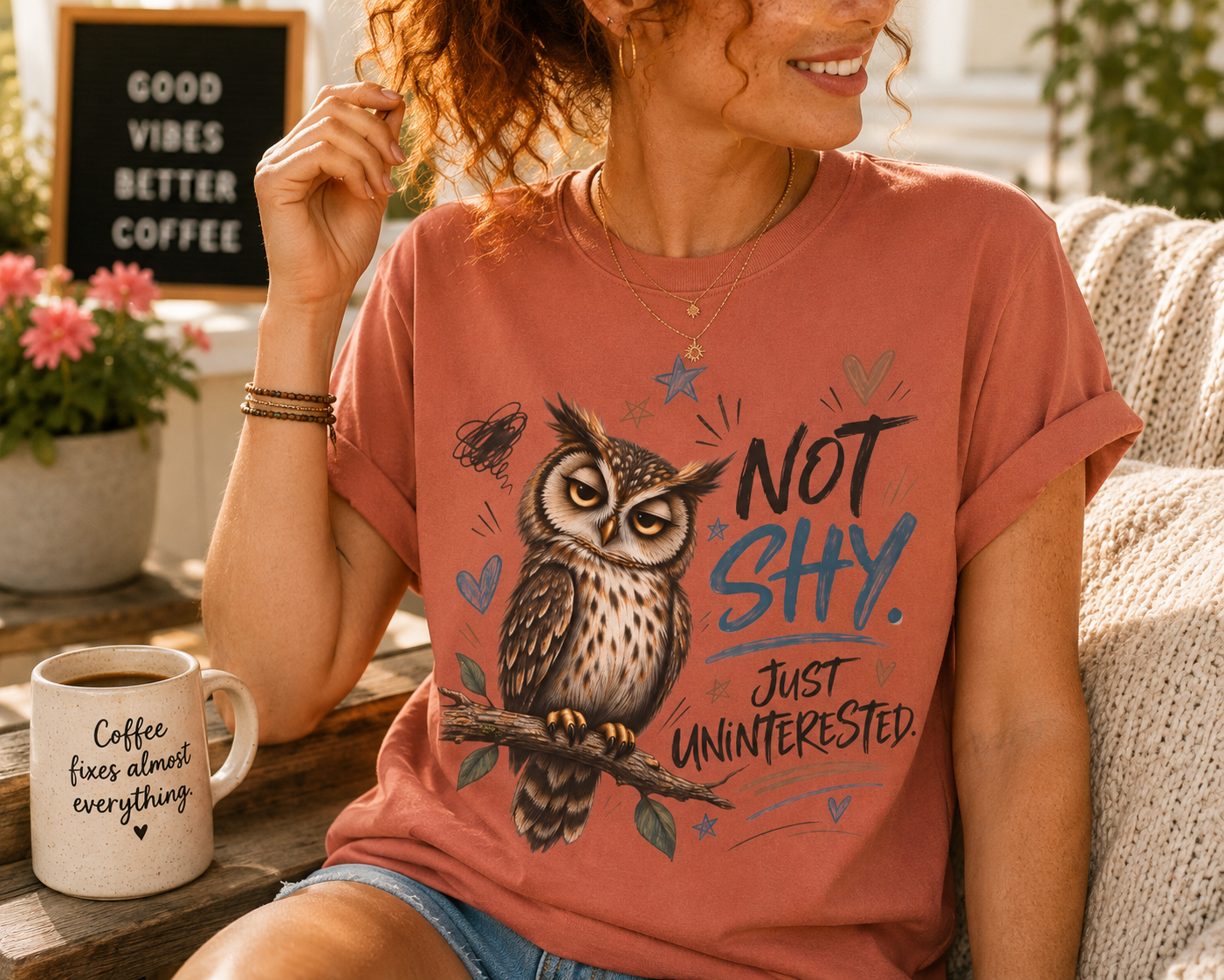 A woman wearing a terracotta-colored graphic t-shirt with an owl illustration and the text 'NOT SHY. JUST UNINTERESTED.